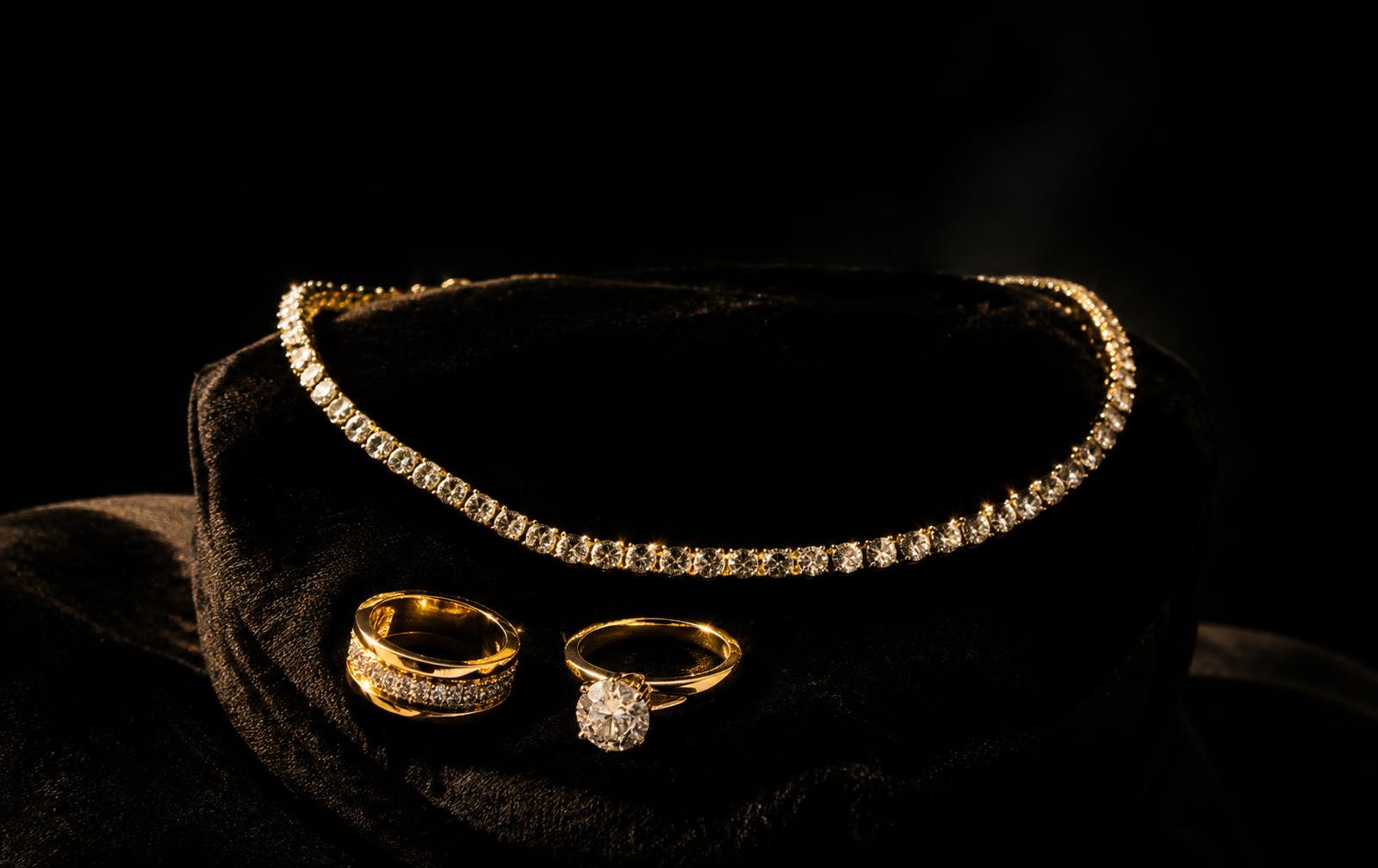 Diamond tennis necklace and gold rings on black velvet